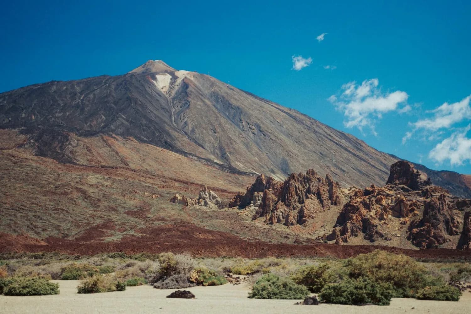 Vulkanische Berglandschaft mit Pico del Teide auf Teneriffa, rauen Felsformationen, trockenem Buschwuchs und blauem Himmel