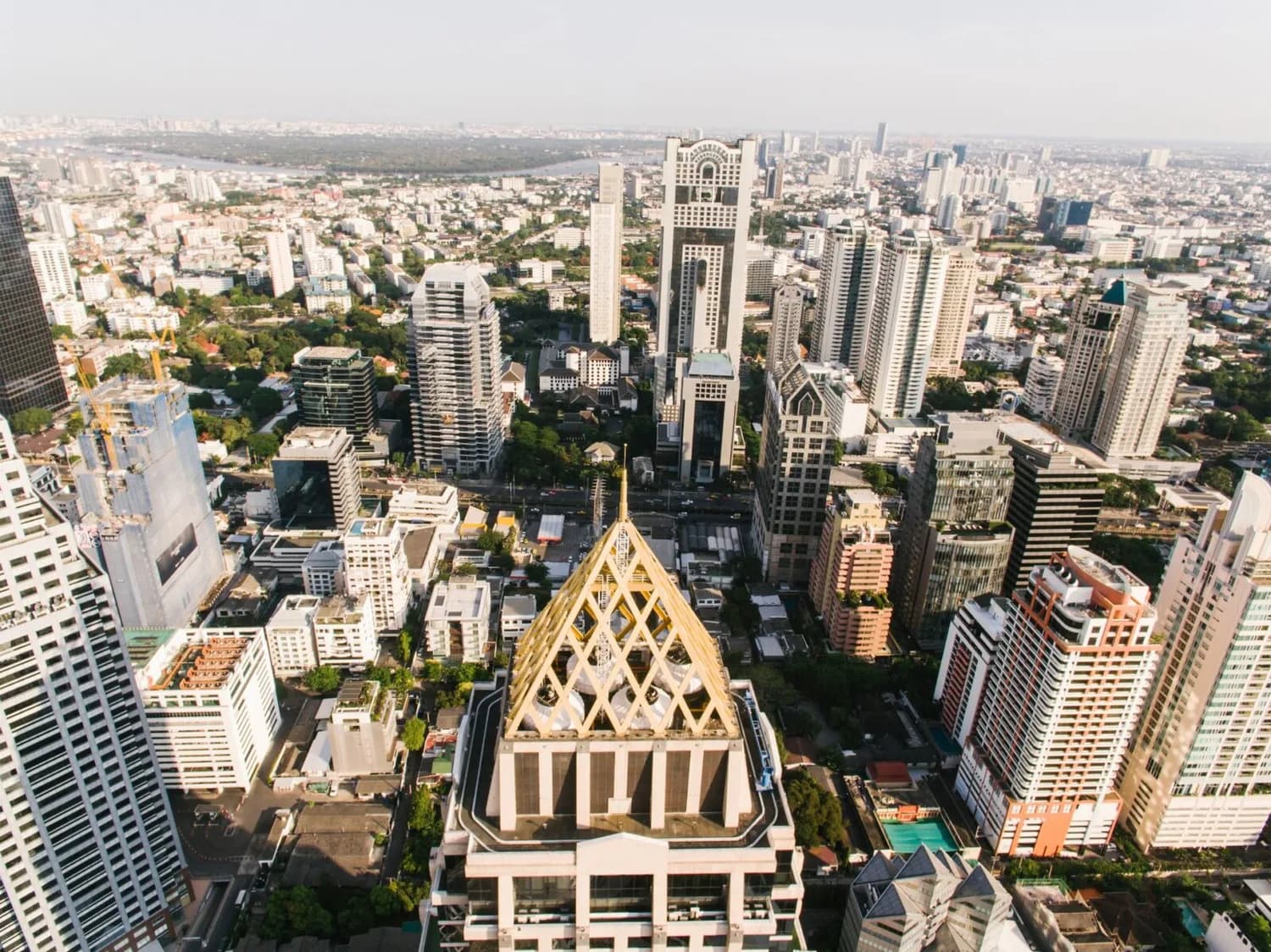 Drohnenaufnahme von Bangkok Skyline mit markantem goldenen Turmaufsatz, Hochhäusern, Bürogebäuden und städtischen Wohnvierteln in Thailand