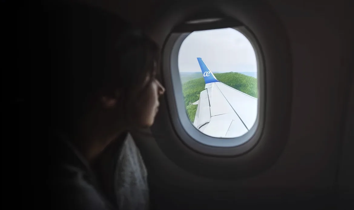 Blick aus einem Flugzeugfenster auf die Tragfläche mit blauem Winglet und Air Europa Logo, Passagier im Sitz betrachtet grüne Landschaft unter dem Flugzeug