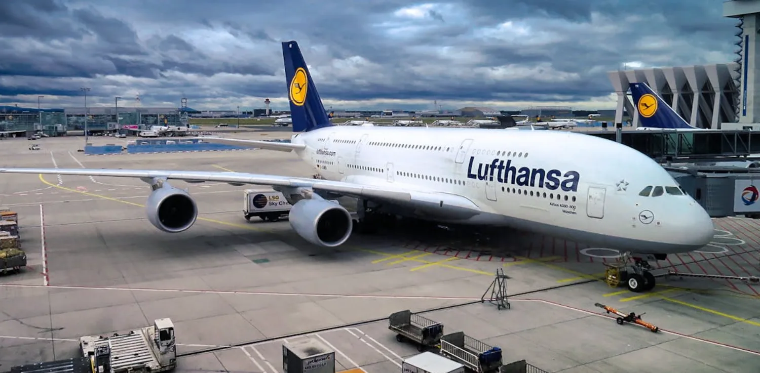 Lufthansa Airbus A380 geparkt am Gate am Flughafen München mit Bodenfahrzeugen und Terminal im Hintergrund