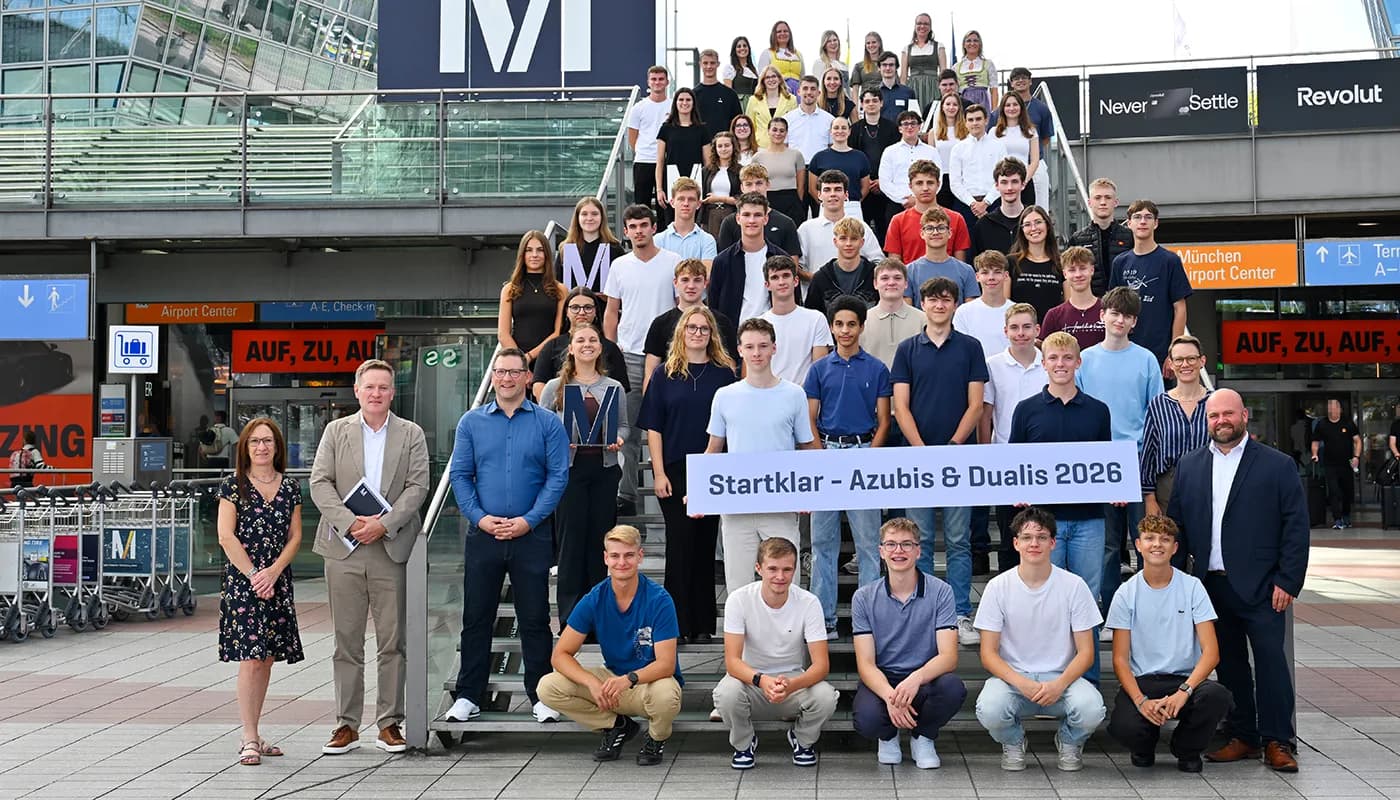 Gruppenfoto von Auszubildenden und Dualis mit Betreuern am Flughafeneingang, Jugendliche halten Banner Startklar – Azubis & Dualis, Begrüßung am Flughafen FJS, Startjahr 2026