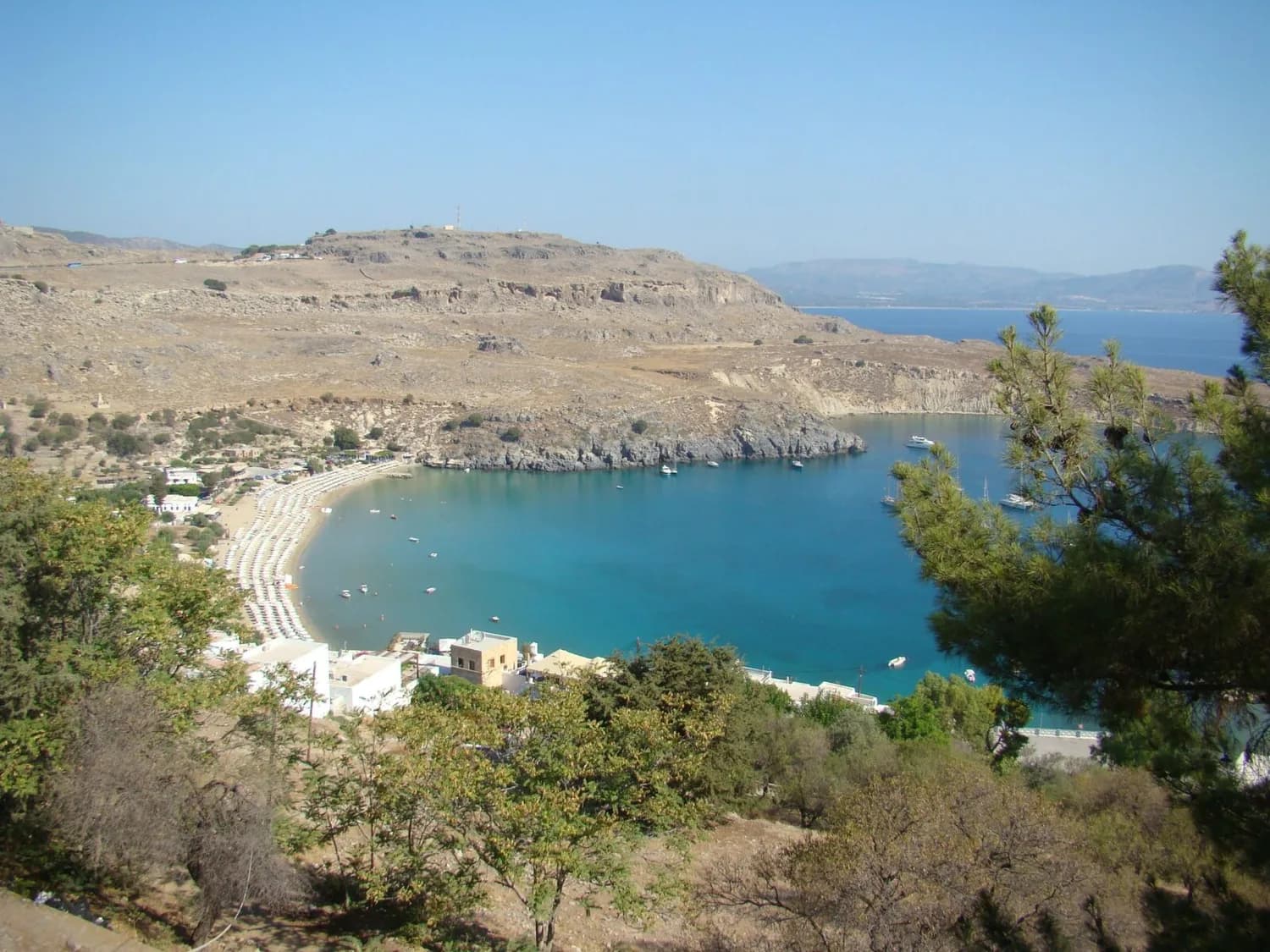 Lindos Bucht auf Rhodos mit blauem Meer, sandigem Strand, Sonnenschirmen und Booten in einer geschützten Bucht