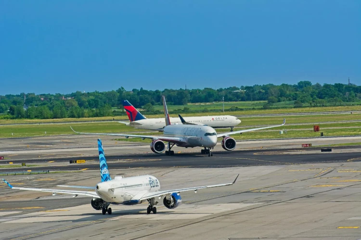geschäftiger Flughafen mit mehreren Taxienden und startbereiten Verkehrsflugzeugen von JetBlue, Virgin und Delta auf Rollwegen und Startbahn