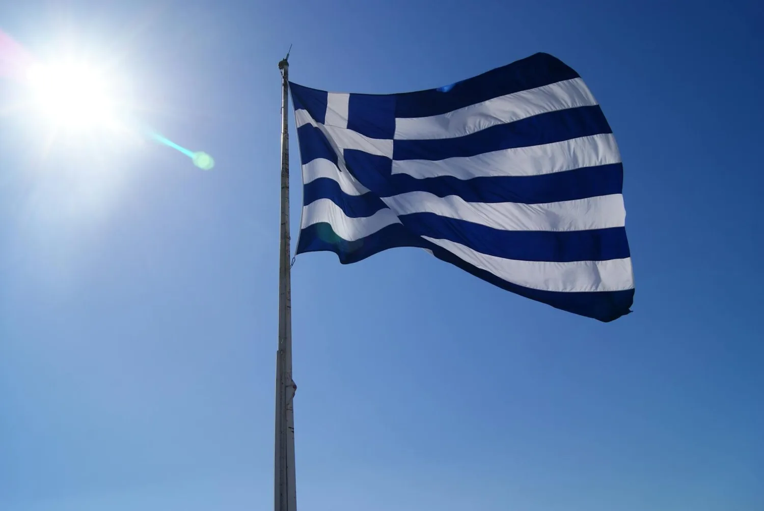 Griechische Flagge blau-weiß weht im Wind vor sonnigem Himmel, Symbol für Flug nach Griechenland ab München