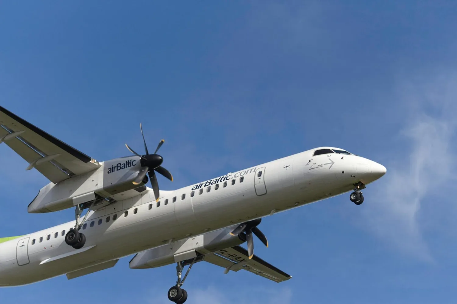 airBaltic Turboprop-Flugzeug beim Landeanflug vor blauem Himmel, Strecke München nach Tallinn Riga Vilnius, Sicht auf Propeller, Fahrwerk und Kabinenfenster