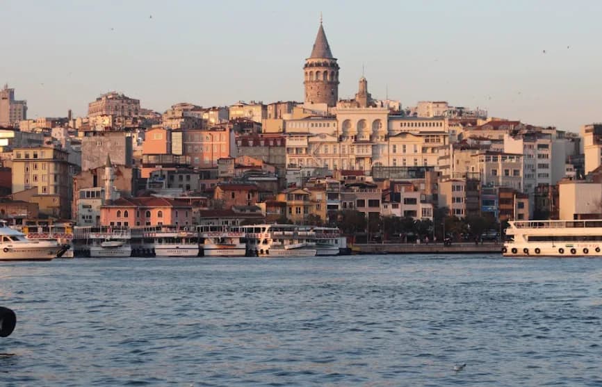 Blick auf Istanbuls Galataturm und dicht bebautes Ufer mit Anlegebooten auf dem Bosporus bei Abendlicht