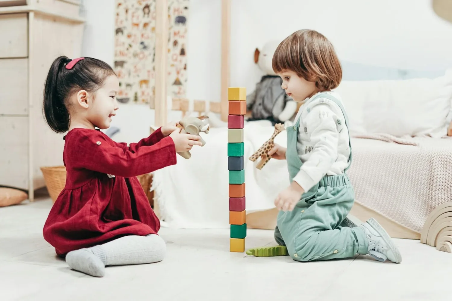Zwei Kleinkinder in Kita am Flughafen München spielen sitzend mit Bauklötzen und Holzspielzeug, Turm aus bunten Würfeln im Zimmer