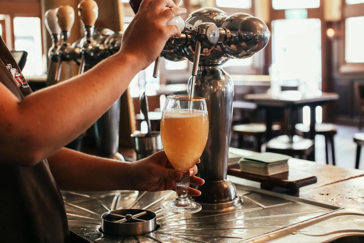 Kellner zapft helles Airbeau-Bier ins Glas an einer Zapfanlage im Münchner Flughafen bei frühlingshaftem Ambiente