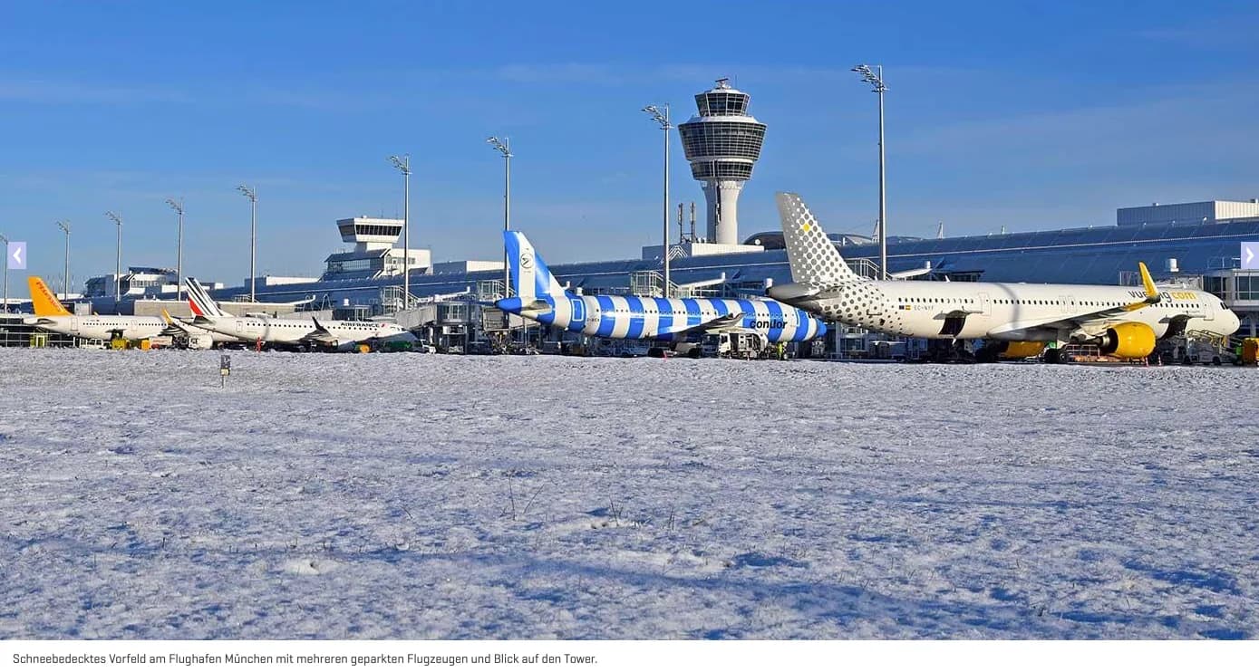 Schneebedecktes Vorfeld am Flughafen München mit mehreren geparkten Passagierflugzeugen und Kontrollturm im Hintergrund