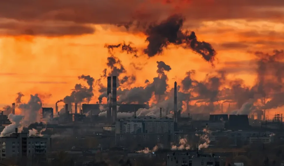 Industrieanlagen mit rauchenden Schornsteinen vor orangefarbenem Himmel, symbolisch für CO2-Emissionen und Luftverschmutzung bei Lufthansa Group Themen