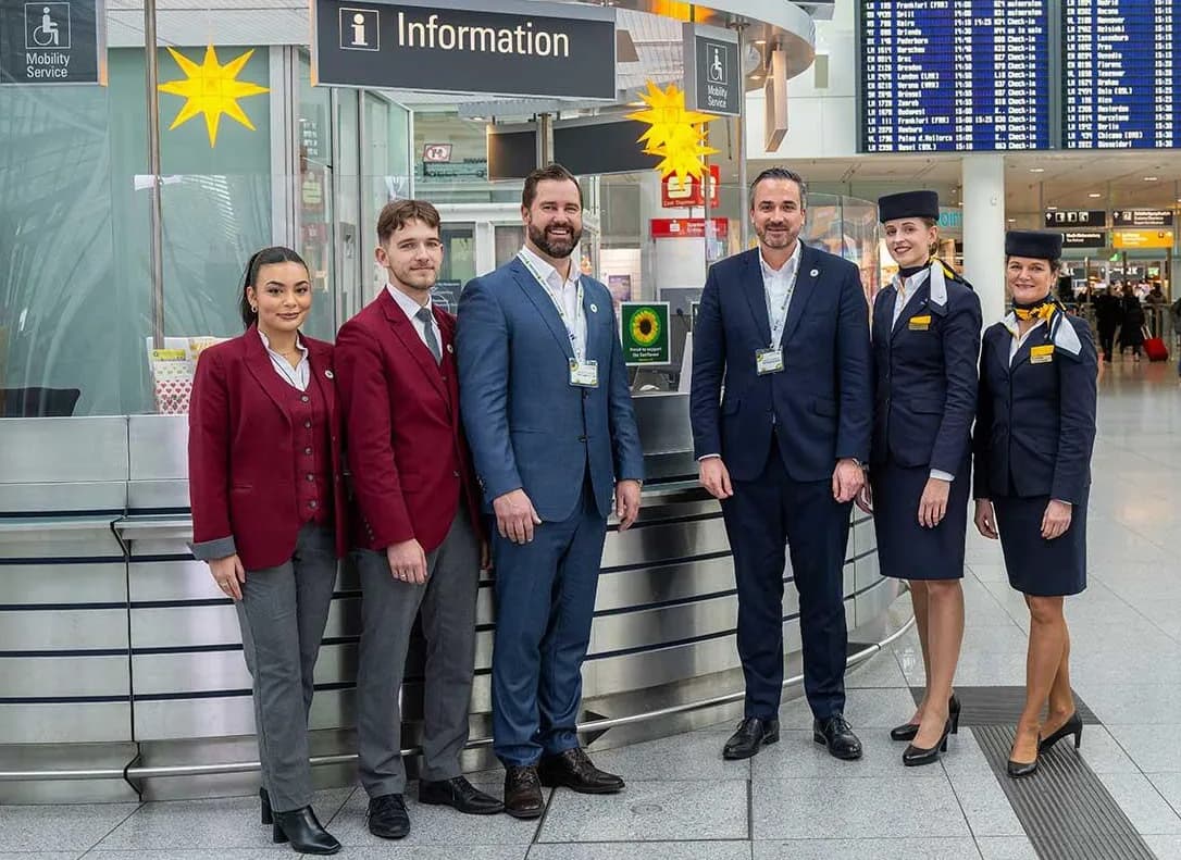 Mitarbeiterinnen und Mitarbeiter am Informationsschalter im Terminal des Flughafens München präsentieren das Sunflower-Programm mit sichtbarem Sunflower-Logo