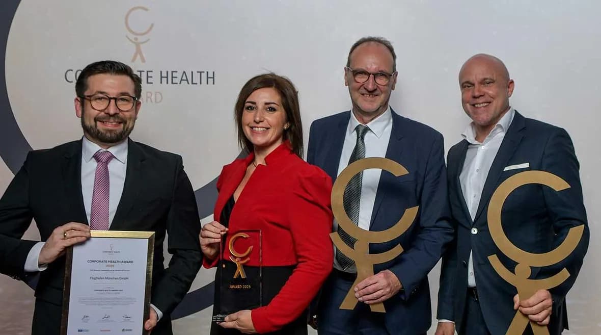 Vier Personen in Businesskleidung halten Corporate Health Award Trophäen und Urkunde bei einer Preisverleihung