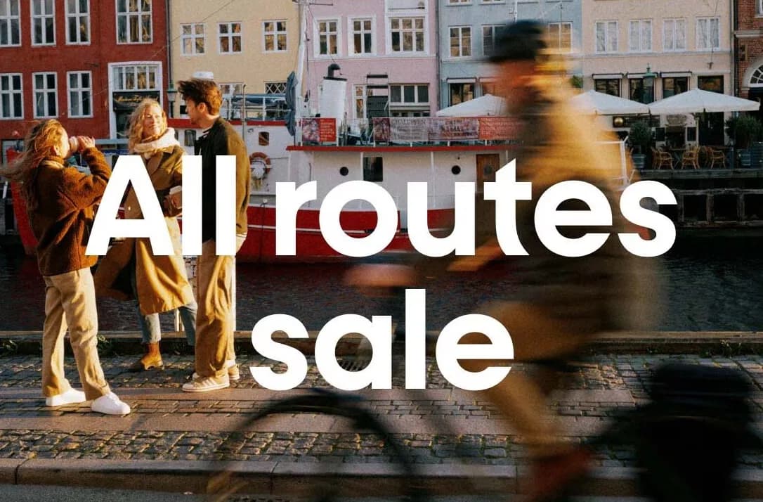 Freundesgruppe am Kai vor bunten Gebäuden und Boot in Kopenhagen mit Schriftzug All routes sale – Werbung für Norwegian günstige Flüge von München nach Skandinavien