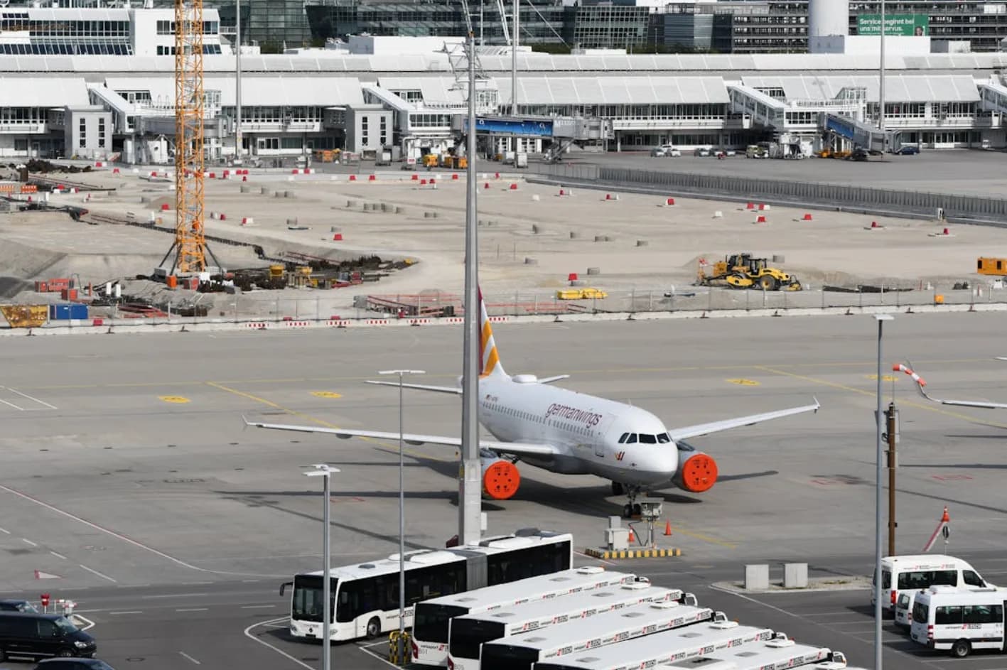 Flughafen München Vorfeld mit geparktem Passagierflugzeug, Busse im Vordergrund und Baustelle an Gates im Hintergrund