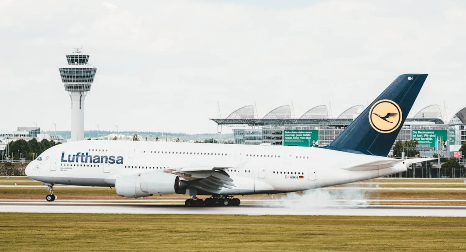 Lufthansa Airbus A380 beim Aufsetzen auf der Landebahn vor Tower und Terminal am Flughafen München