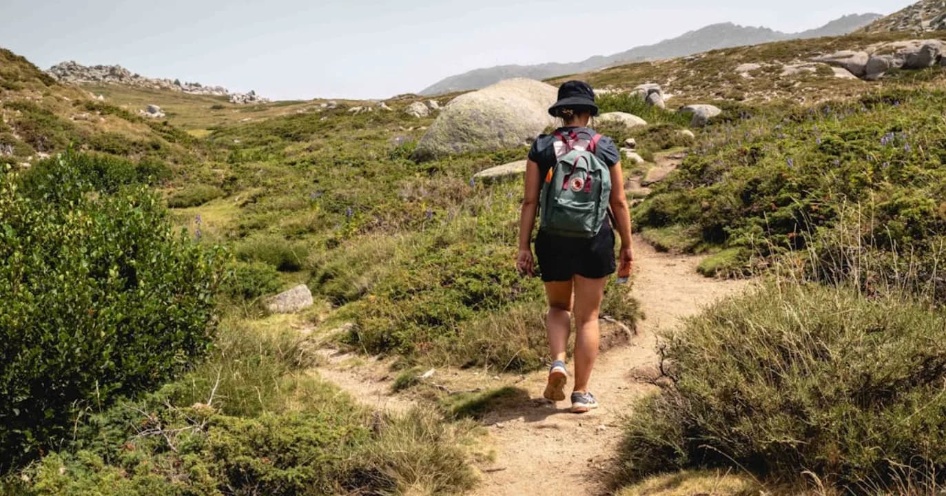 Wanderin mit Rucksack auf Pfad durch karge korsische Berglandschaft bei klarer Sicht