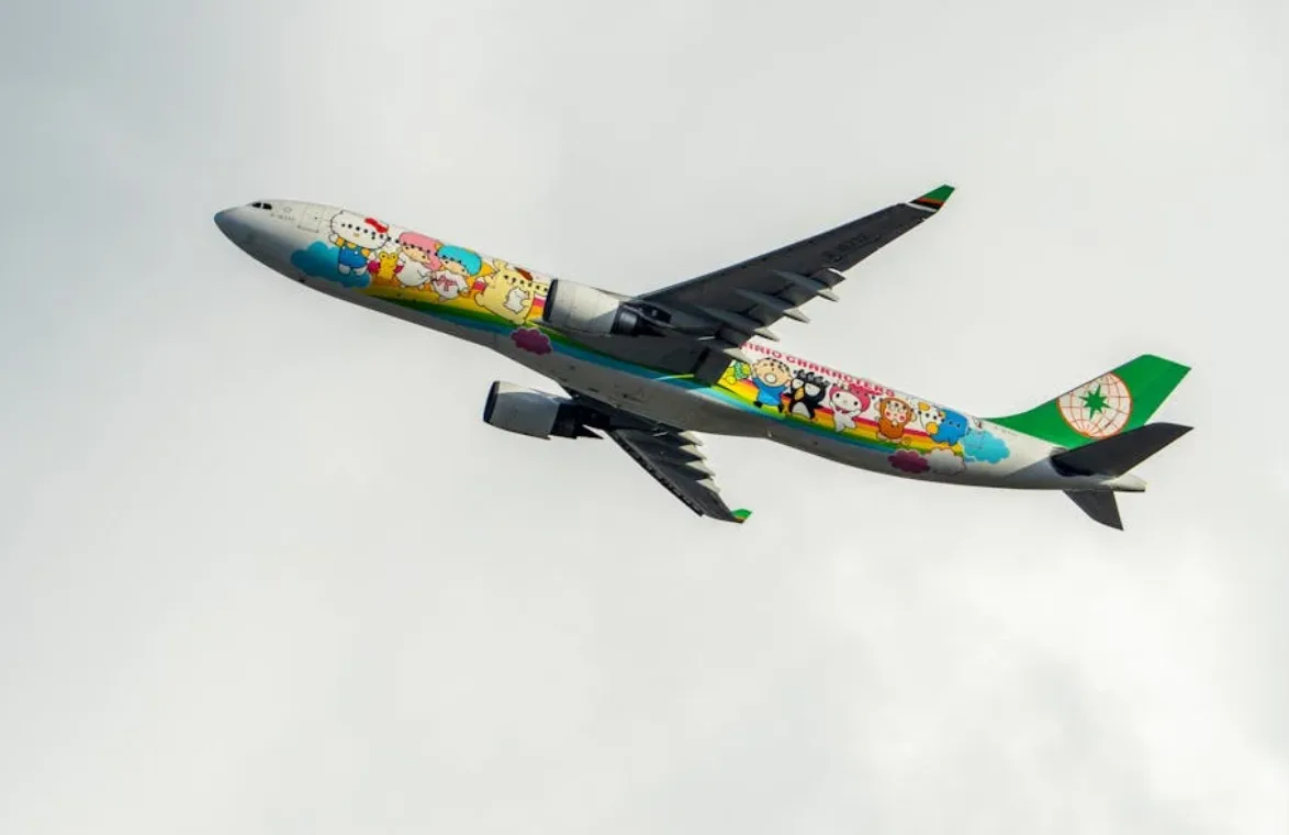 Passagierflugzeug mit bunten Cartoon-Charakteren und grünem Leitwerk fliegend vor hellgrauem Himmel