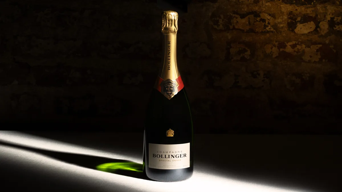 Flasche Bollinger Champagner auf Tisch mit Lichtspot vor dunkler Mauer, elegante Produktaufnahme