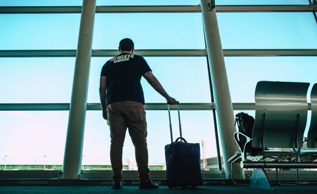 Reisender mit Rollkoffer am Fenster im Flughafen München, Blick auf Rollfeld und Terminalgebäude
