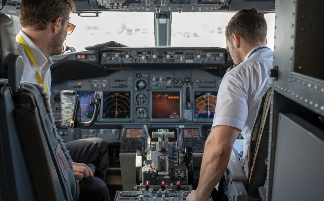 Cockpit eines Verkehrsflugzeugs mit zwei müden Piloten, Blick auf Instrumententafel, Steuerknüppel und Navigationsdisplays