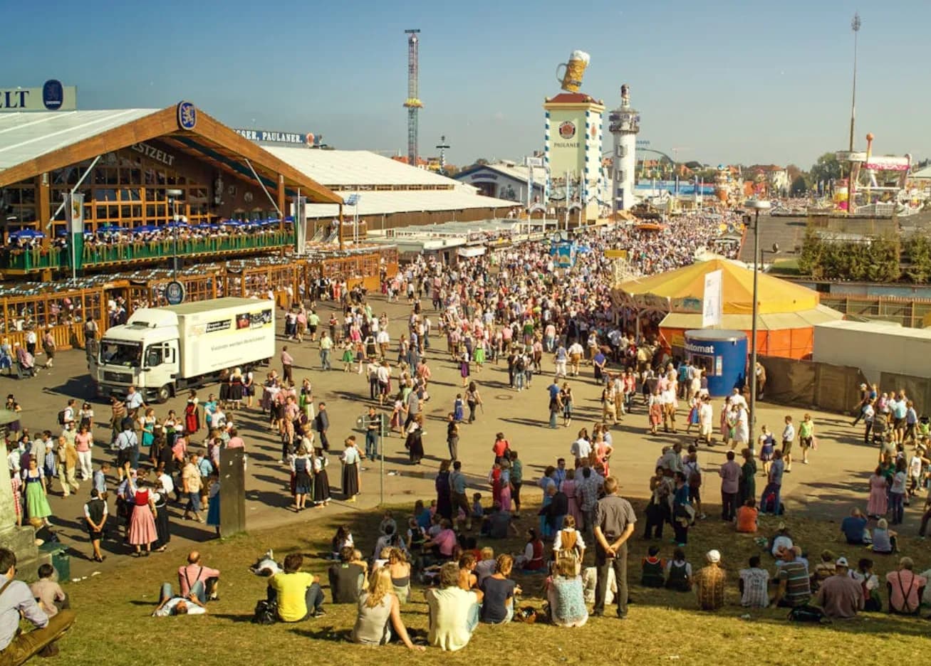 Belebtes Oktoberfest-Gelände mit Festzelt, Fahrgeschäften und Besuchern in Trachten am Flughafen München ParkSleepFly