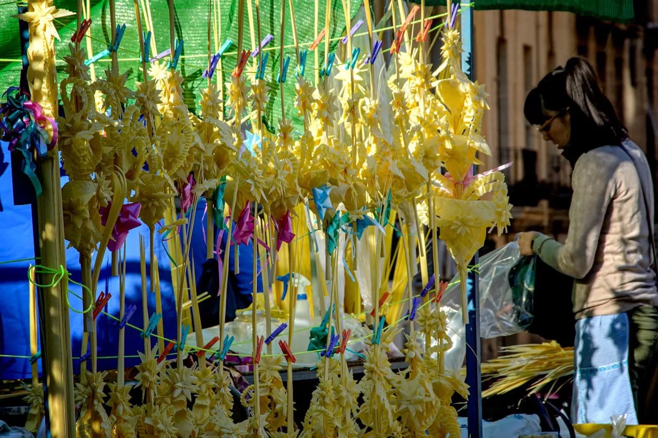 Marktstand mit handgefertigten gelben Palmwedel-Dekorationen an Stäben, bunte Wäscheklammern und eine Person im Hintergrund
