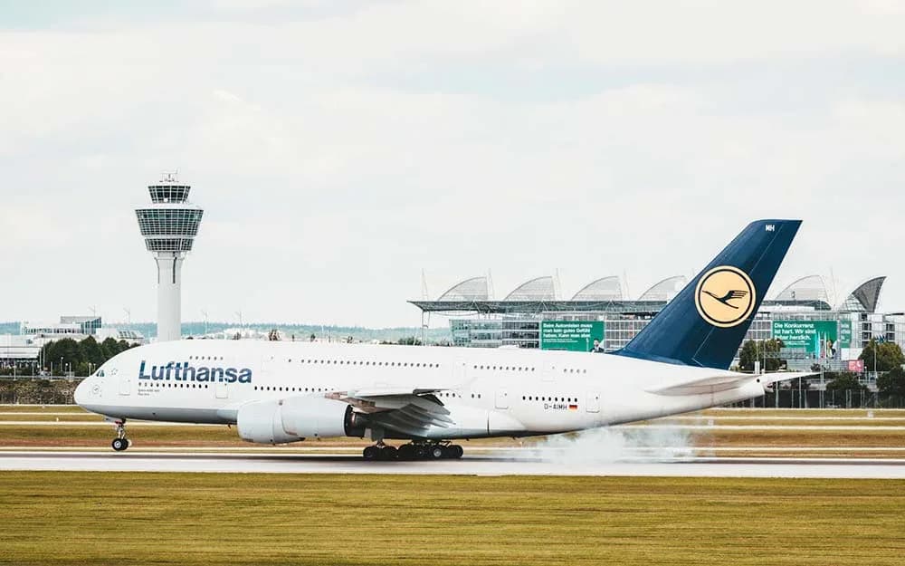 Lufthansa Flugzeug landet auf der Rollbahn vor Tower und Terminal am Münchner Flughafen, mit Hinweis auf Parkmöglichkeiten