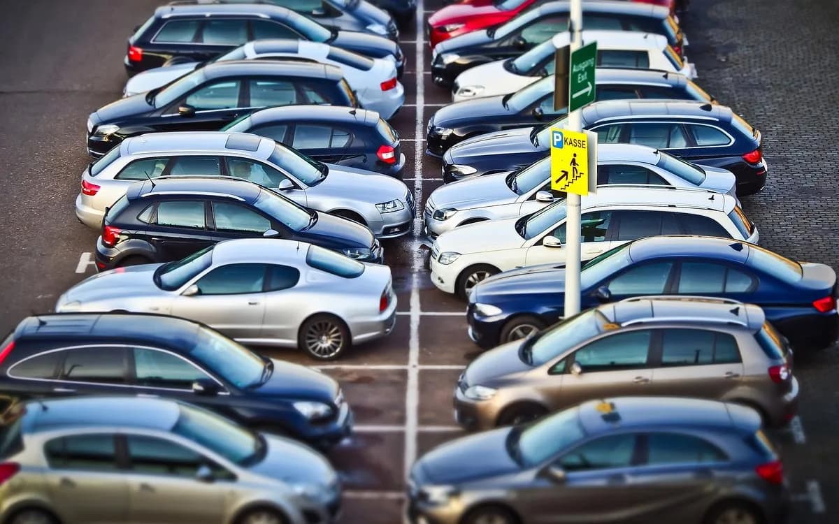 Voll besetzter Parkplatz mit geparkten Autos in Reihen, Parkplatzschild mit Kasse und Richtungspfeil im Vordergrund