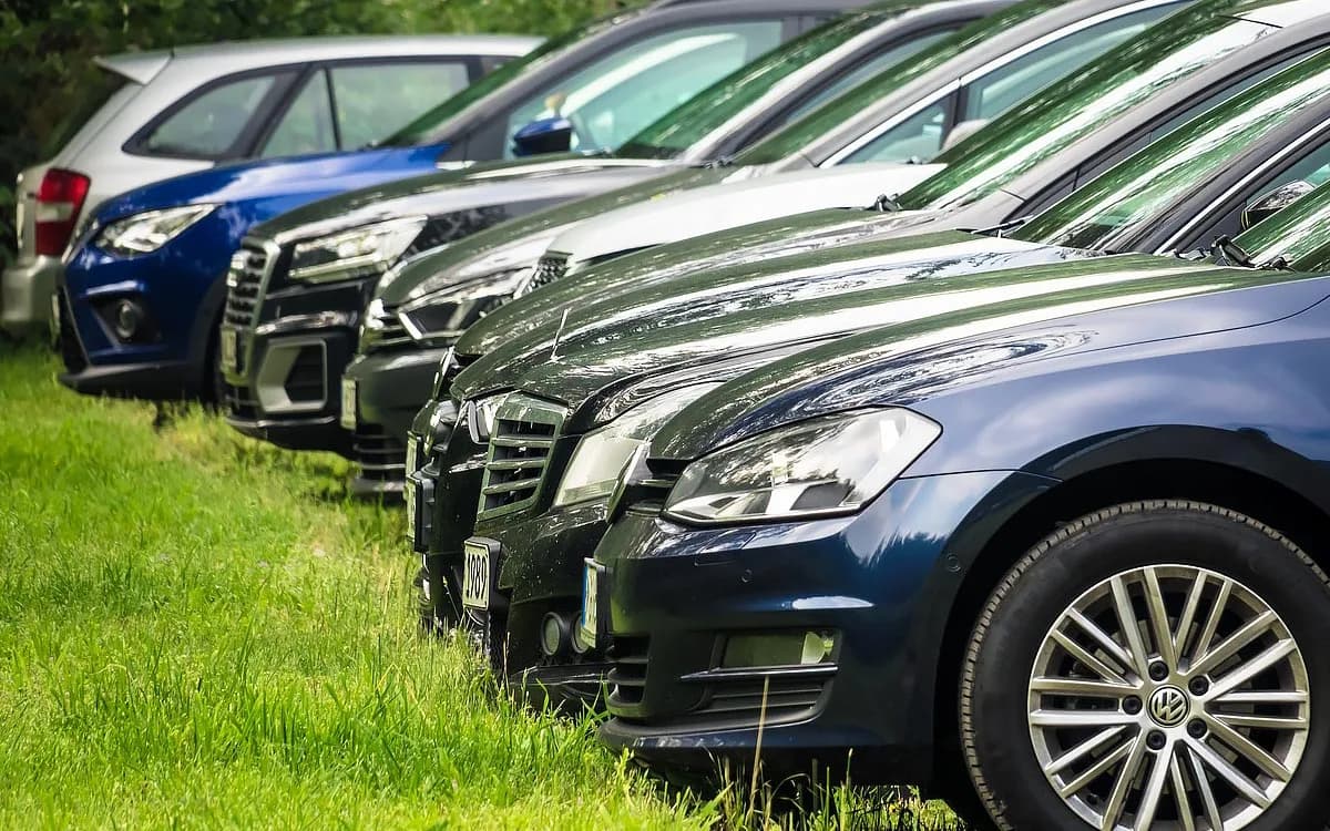 Mehrere geparkte Autos nebeneinander auf einer Wiese bei einem Bauernhofparkplatz nahe München