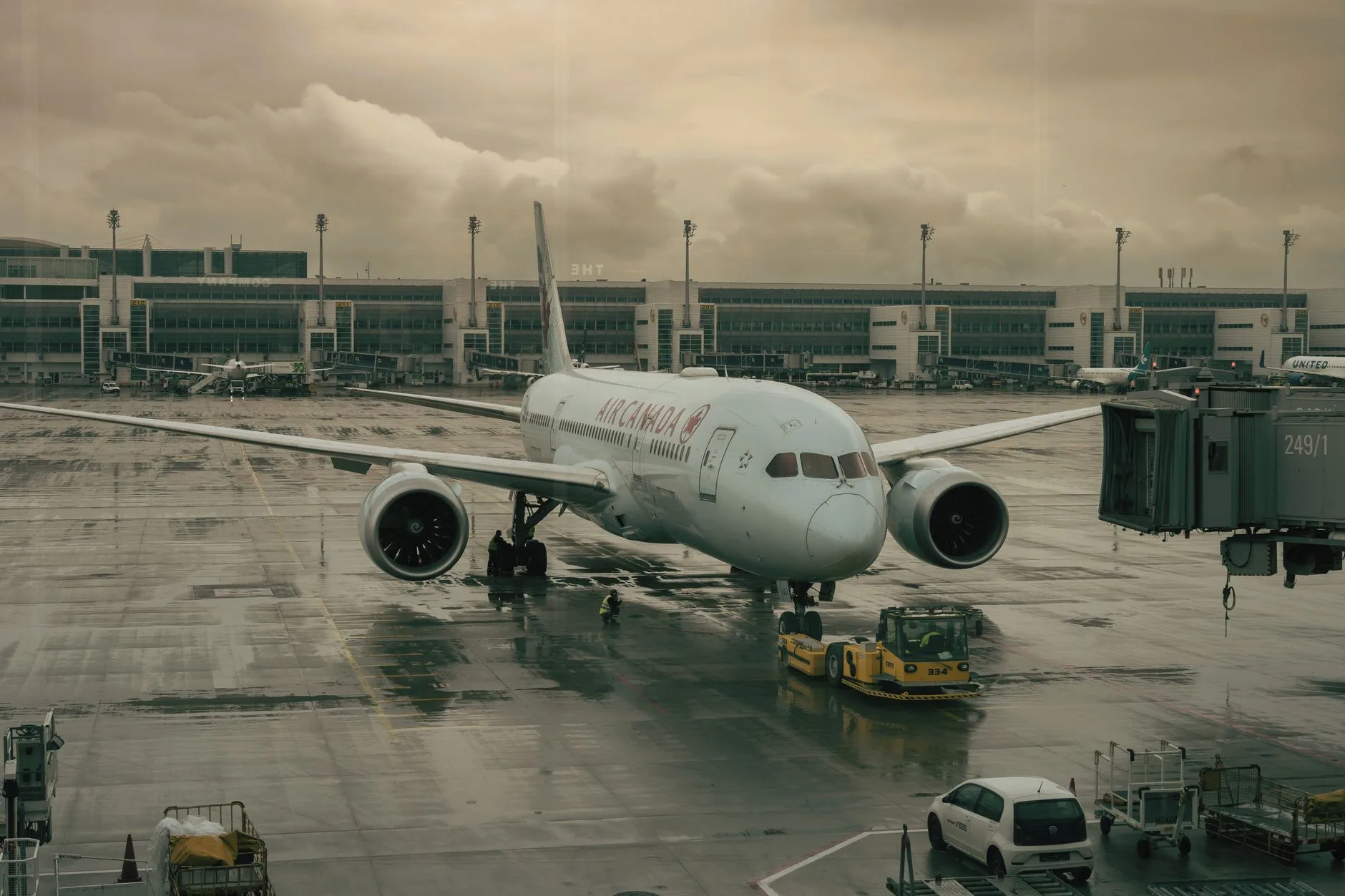 Air Canada Flugzeug wird bei Regenwetter auf dem Vorfeld von einem Schlepper vom Terminal weggezogen