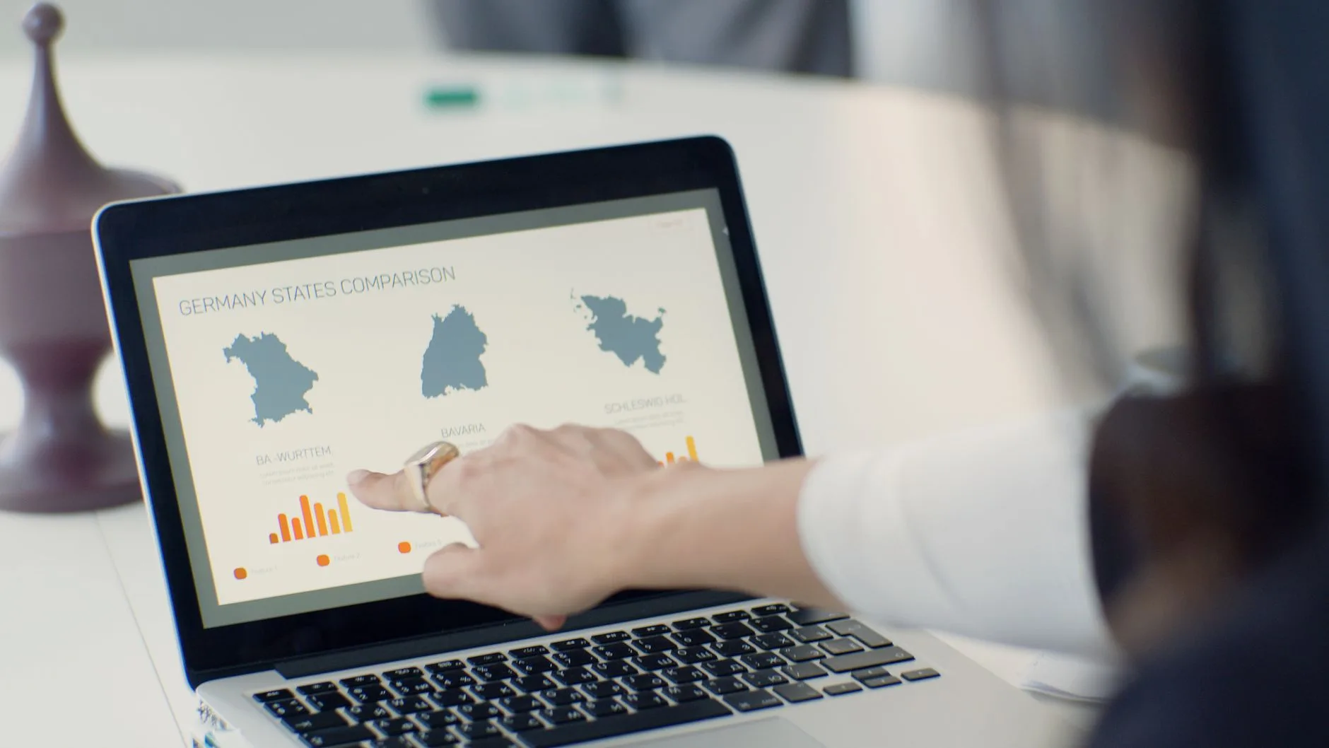 Hand zeigt auf Laptop-Bildschirm mit Vergleich deutscher Bundesländer und Balkendiagrammen