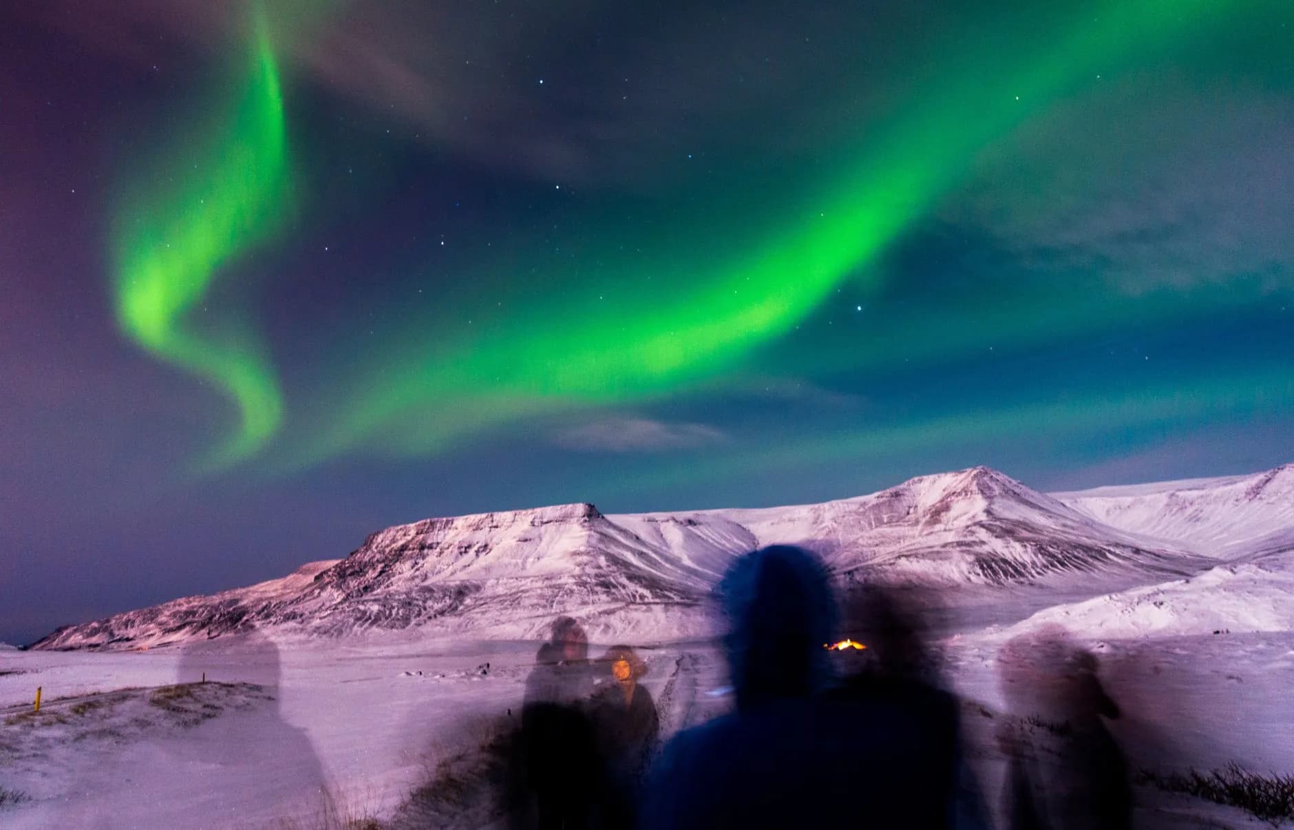 Grüne Polarlichter über schneebedeckten Bergen, im Vordergrund Silhouetten mehrerer Betrachter