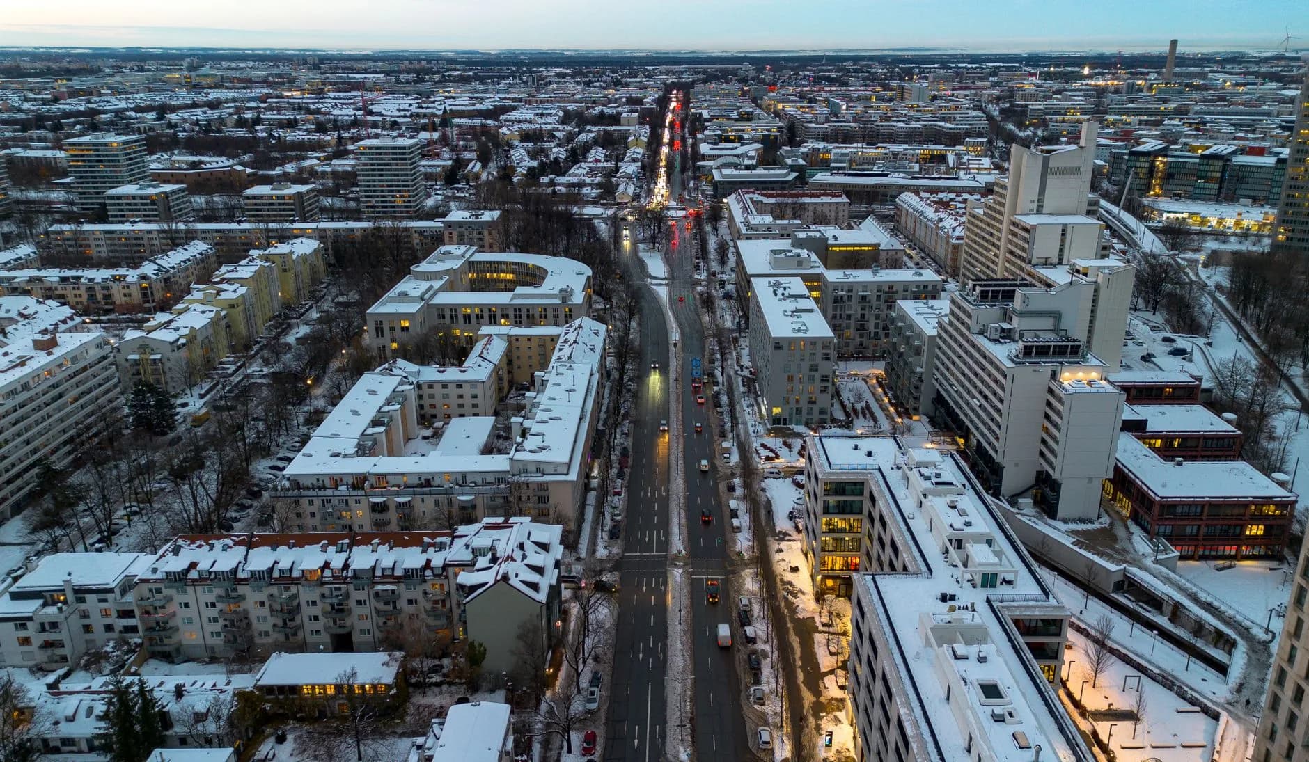 Luftaufnahme einer verschneiten Stadt mit beleuchteter Hauptstraße und dichter Bebauung in der Abenddämmerung