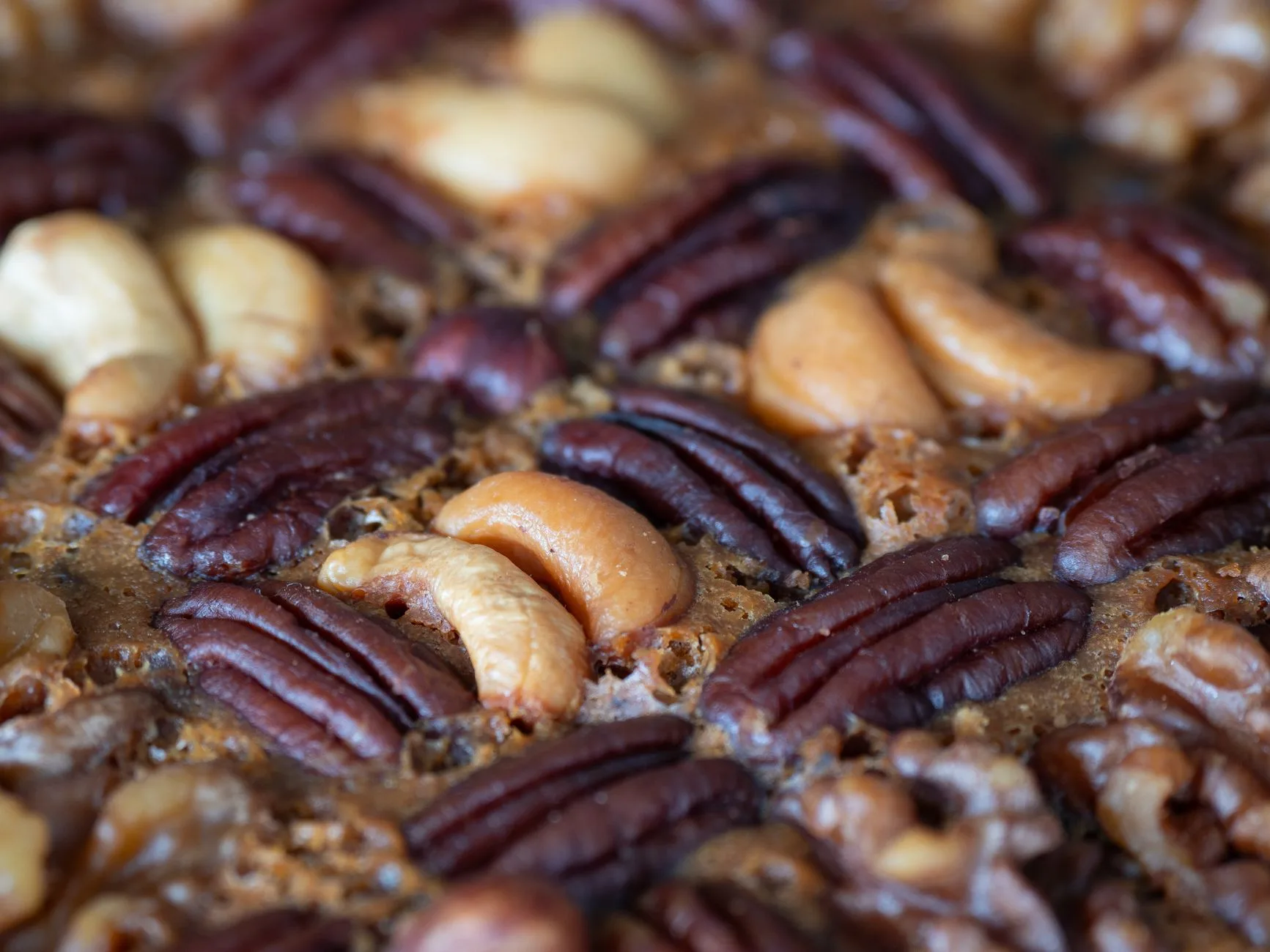 Nahaufnahme von Pekannüssen und Cashewkernen auf karamellisiertem Gebäckboden