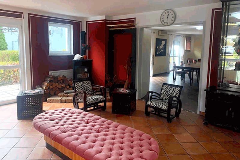 Hotelbereich mit langem rosa Polsterbänkchen, zwei Sesseln mit Zebra-Bezug, Holzstapel und Durchgang zu einem Speiseraum.