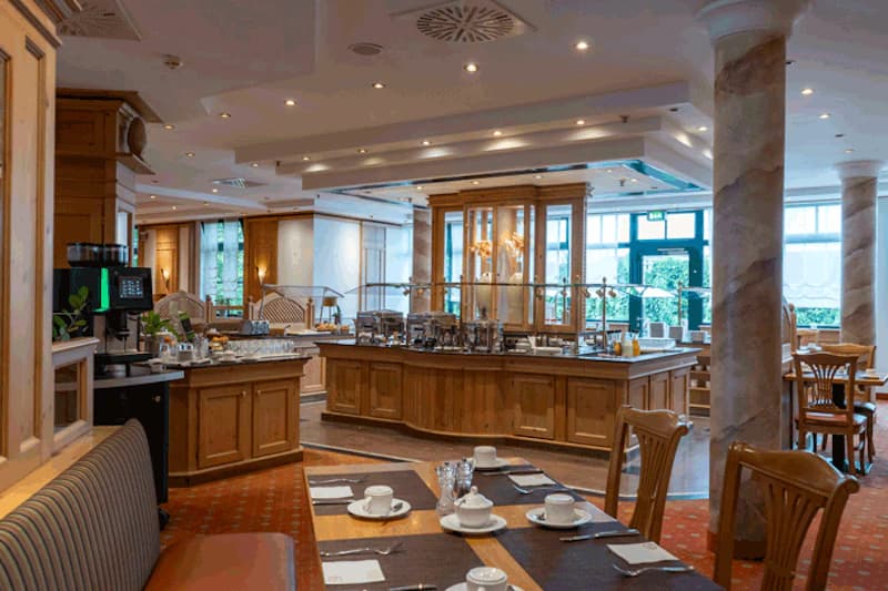 Restaurantbereich mit Buffetinsel, gedeckten Tischen, Kaffeeautomaten und Holzmöbeln.