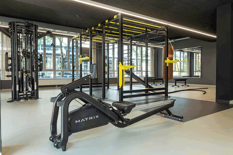 Fitnessraum mit Rudergerät MATRIX, Trainingsrahmen, Sandsack, Kabelzug und großen Fenstern.