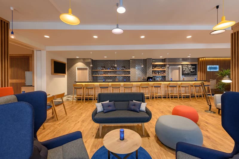 Offener Hotel-Loungebereich mit Sitzgruppen, Bar mit Hockern und Pendelleuchten.