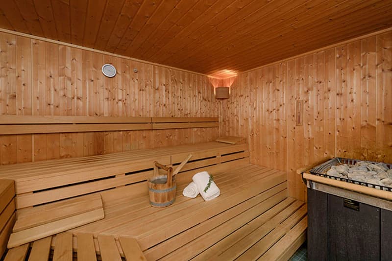 Holzsauna mit gestuften Liegebänken, Saunaofen, Aufgusseimer und zwei aufgerollten Handtüchern.