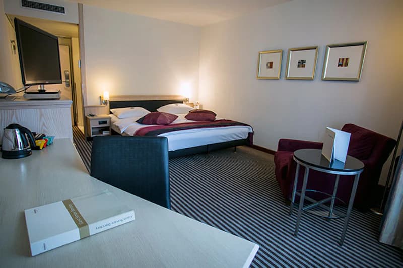 Hotelzimmer mit Doppelbett, Schreibtisch, gestreiftem Teppich und Sitzecke.