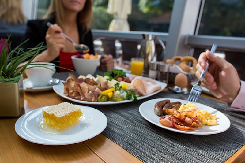 Tisch mit Frühstück: Honigwabe, Aufschnitt, Rührei, Speck, Würstchen und Orangensaft.