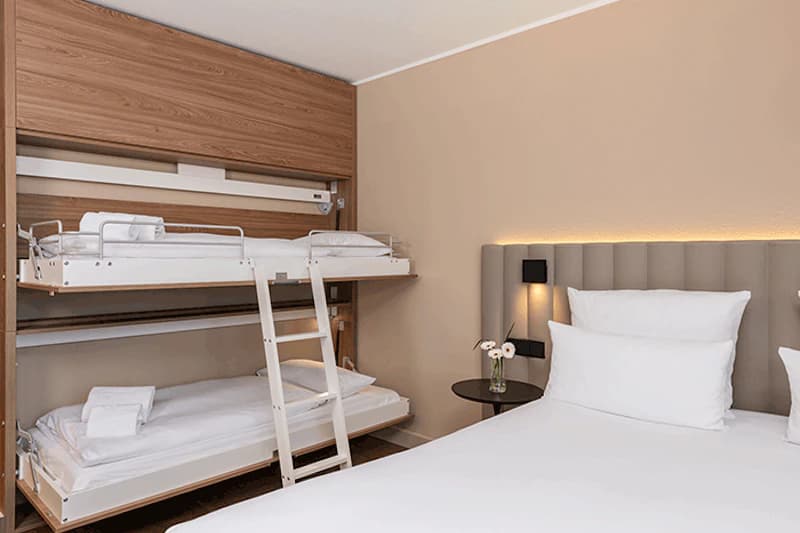 Doppelbett rechts und Etagenbett links mit Leiter, Nachttisch mit Vase und Wandbeleuchtung.