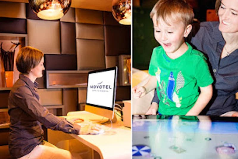 Frau sitzt an Schreibtisch vor Computer mit Novotel-Logo; daneben Mutter und Kind spielen an einem Touchtisch.