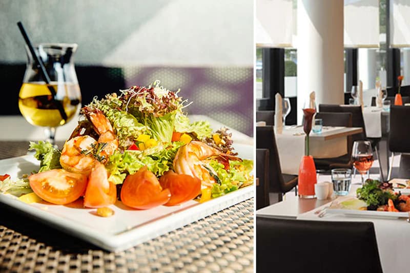 Vorspeisensalat mit Garnelen und Tomaten auf Teller; im Hintergrund gedeckte Tische eines Hotelrestaurants.