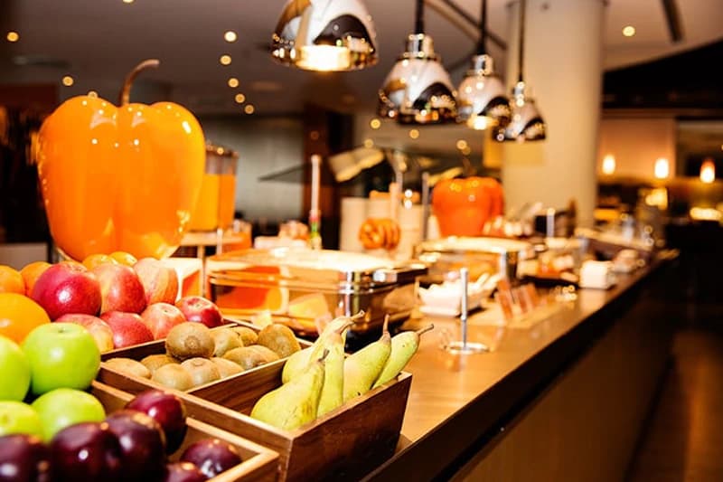 Buffet mit Holzschalen voller Früchte wie Birnen, Äpfel und Kiwis, Warmhaltebehälter und Hängelampen.