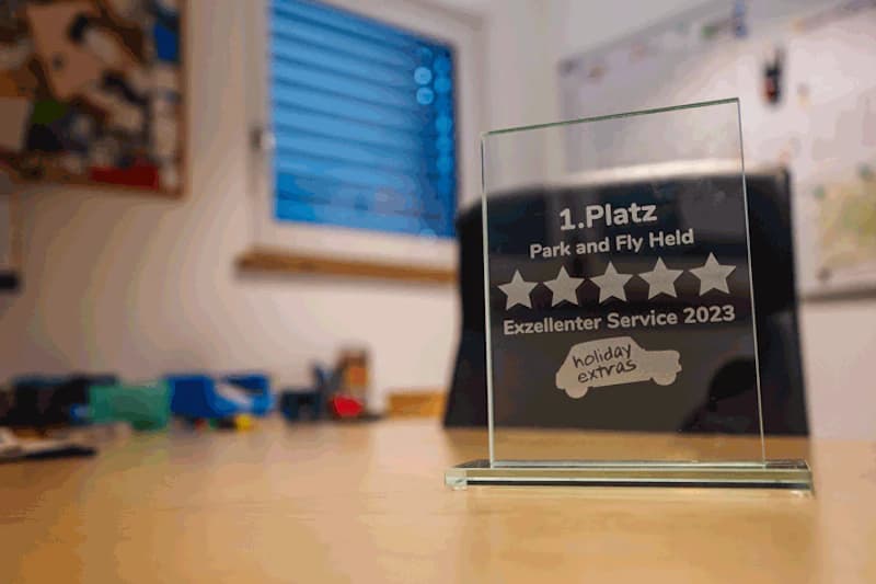 Glasaufsteller mit Gravur 1. Platz Park and Fly Held Exzellenter Service 2023 auf Holztisch, unscharfer Hintergrund.
