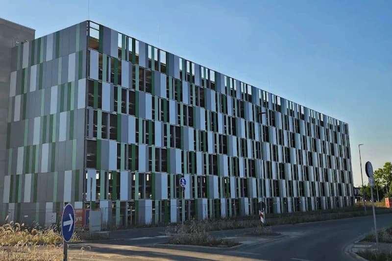 Mehrstöckiges Parkhaus mit gestreifter Fassade aus grünen und weißen Paneelen an einer Zufahrtsstraße mit Verkehrsschildern.
