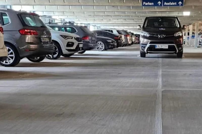 Mehrere Reihen geparkter Autos in einem hellen Betonparkhaus mit Deckenstützen.