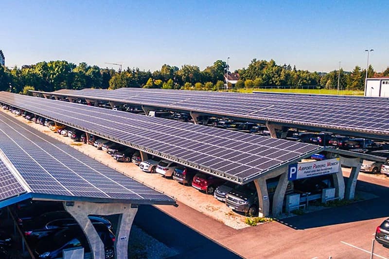 Reihen von Carports mit Solarpaneelen auf den Dächern und geparkten Autos darunter.