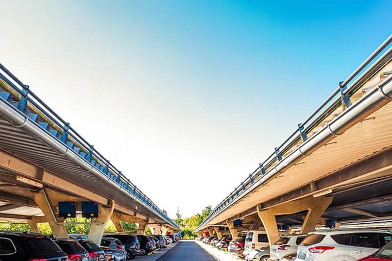 Zwei lange Reihen überdachter Stellplätze mit geparkten Autos und zentraler Fahrspur unter Schutzdächern.